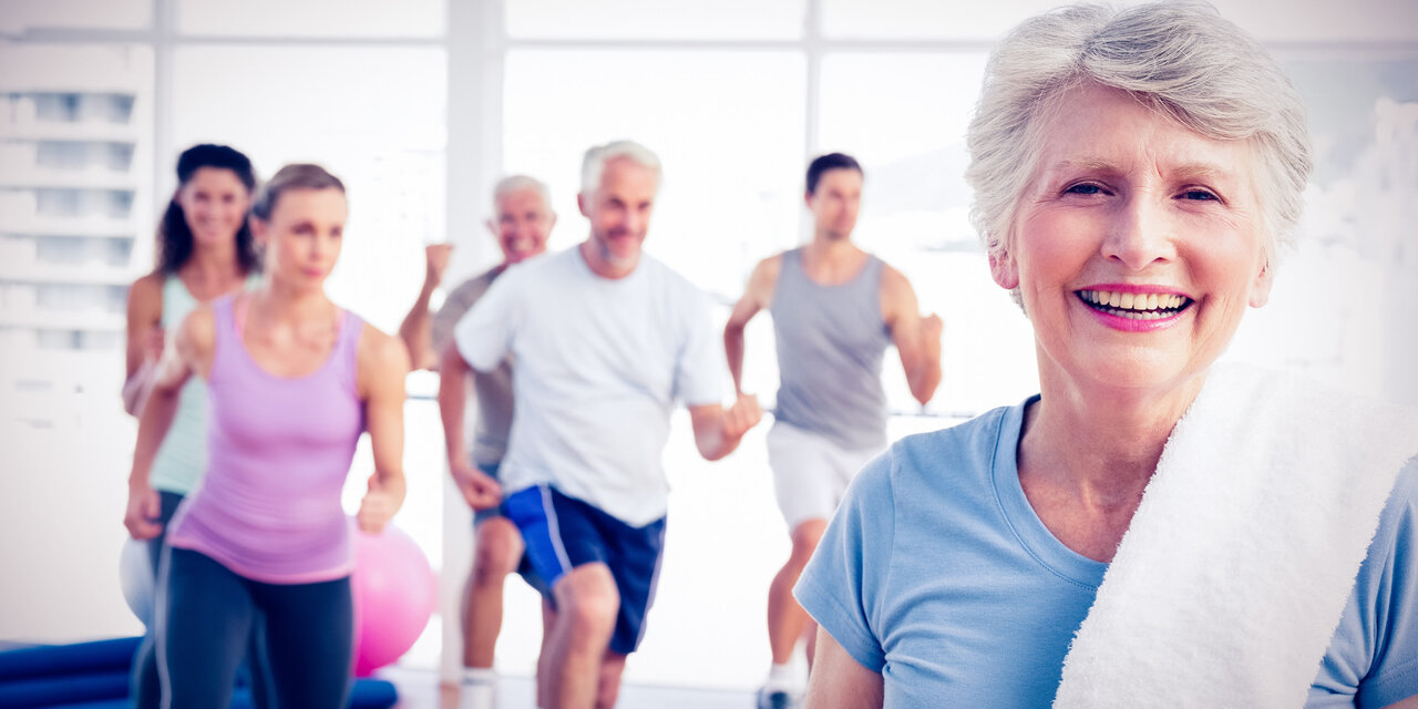 Ältere Frau mit anderen TeilnehmerInnen, die im Fitnessstudio trainieren