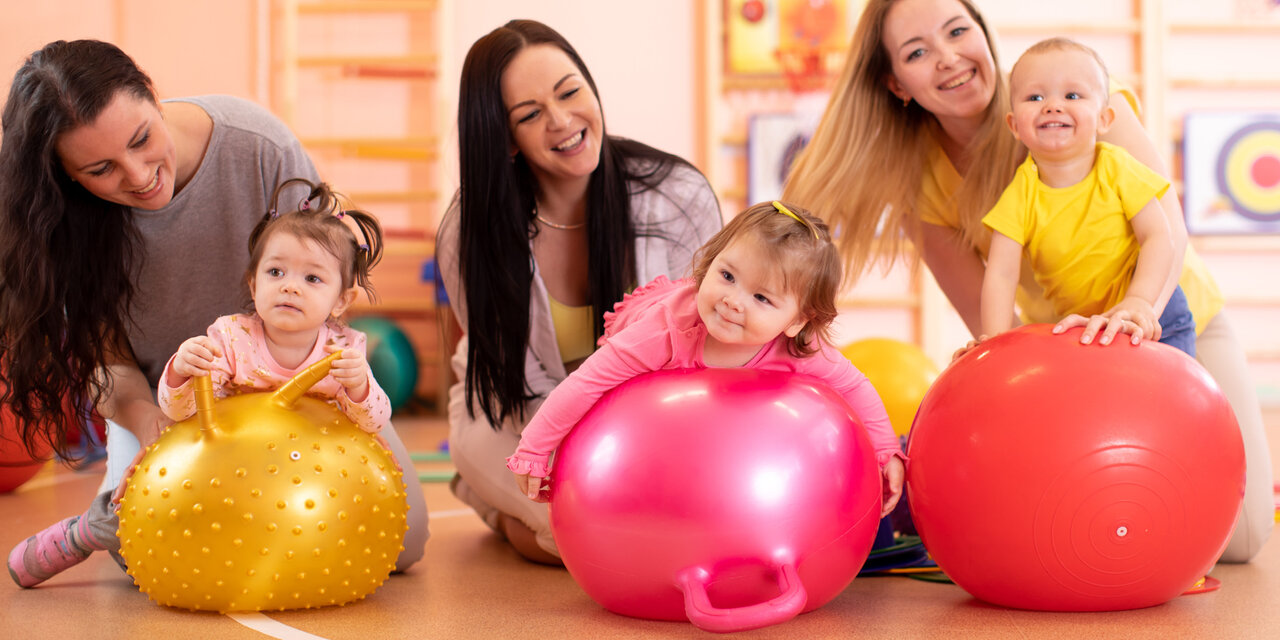 Gruppe von Müttern und ihren Kindern, die auf Gymnastikbällen im Fitnessstudio Yogaübungen machen