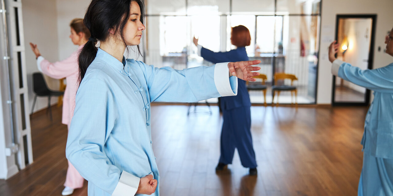 Eine Gruppe von Menschen in chinesischer Kleidung, die während der Qigong-Übung langsame Bewegungen mit rhythmischer Atmung kombinieren.