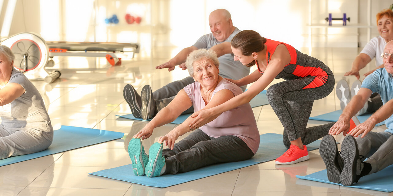 Junger Trainer hilft älteren Menschen beim Training im Fitnessstudio.