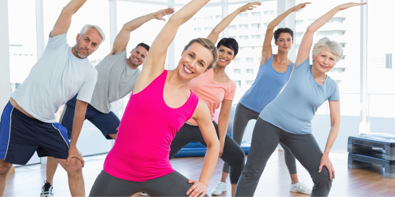 Eine Gruppe an Menschen, die beim Yoga-Kurs die Hände streckt.